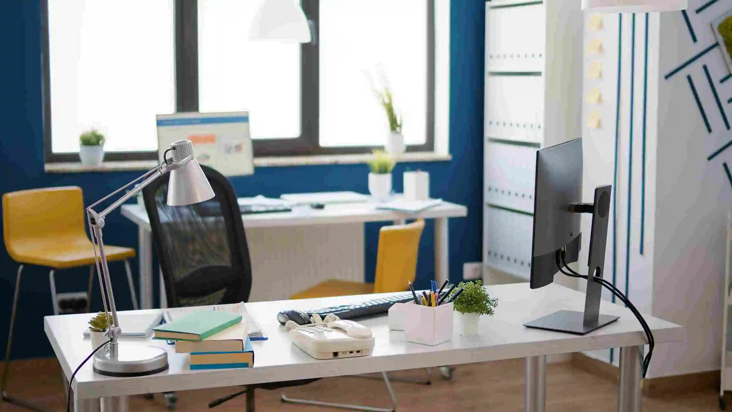 Modern workspace desk with a monitor, lamp, and chair beside a window